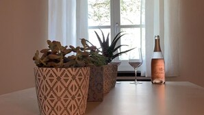 Una habitación con techo de ladrillo, un ventanal con cortinas blancas, tres macetas con plantas y una botella sobre una mesa.
