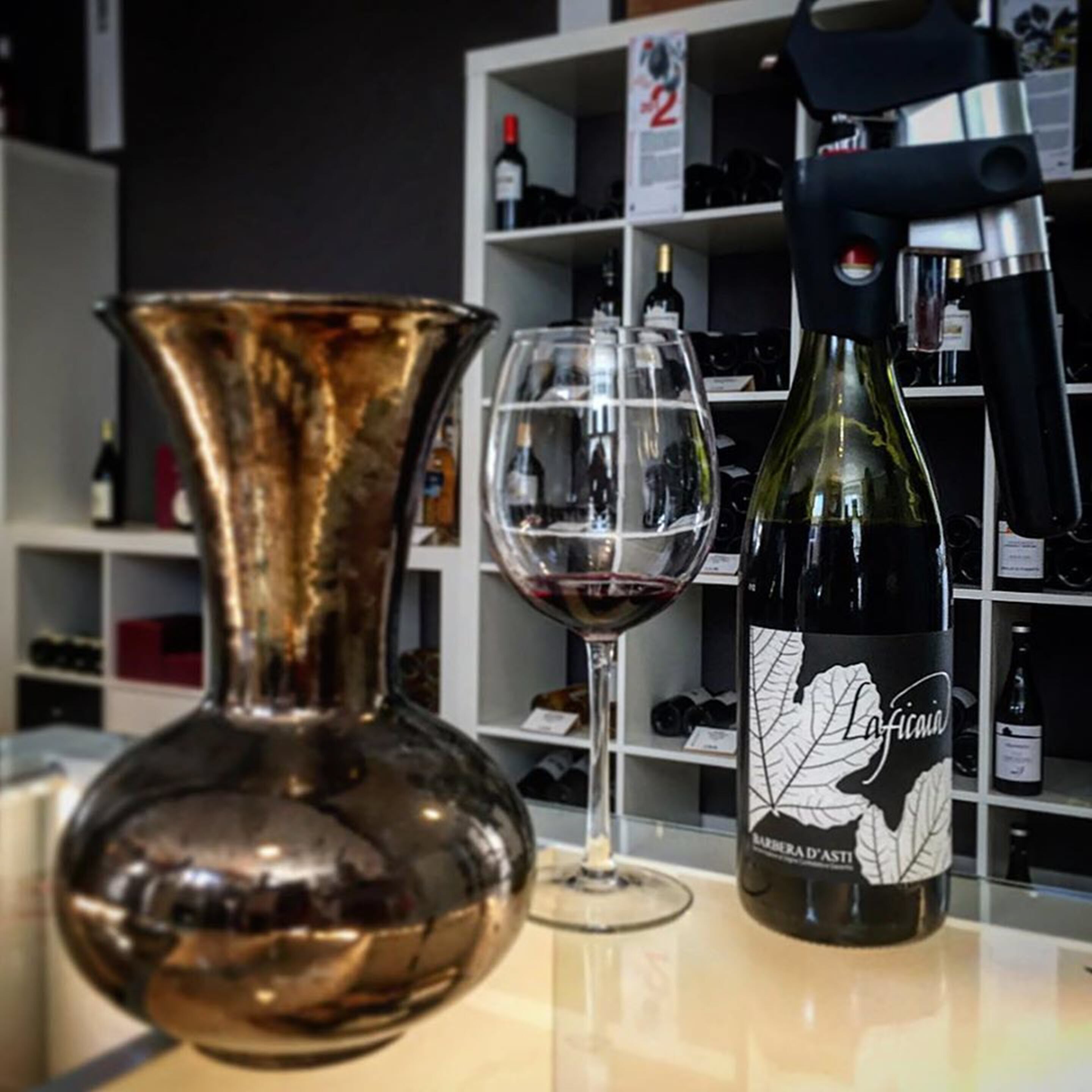 A wine bottle, a wine glass, and a decorative vase on a counter.