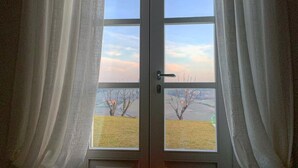 Una habitación con ventana, cortinas y una vela encendida sobre una mesa.