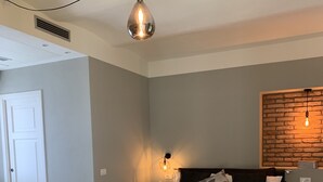 Un dormitorio con cama, luz empotrada, una mesita y una puerta.