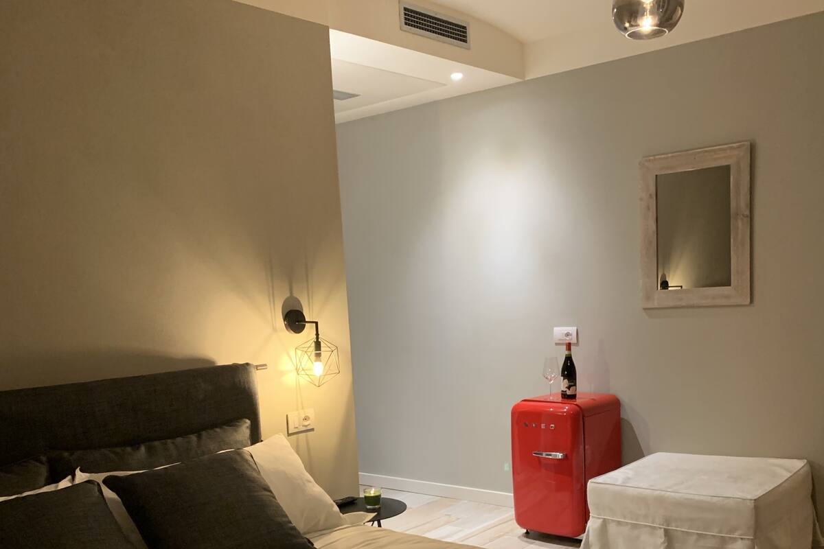 Ein Schlafzimmer mit einem großen Bett, einer roten Kommode, einem kleinen Tisch mit einer Flasche und einem wandmontierten Spiegel.