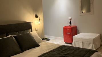 Un dormitorio con una cama grande, un aparador rojo, una mesita con una botella y un espejo instalado en la pared.