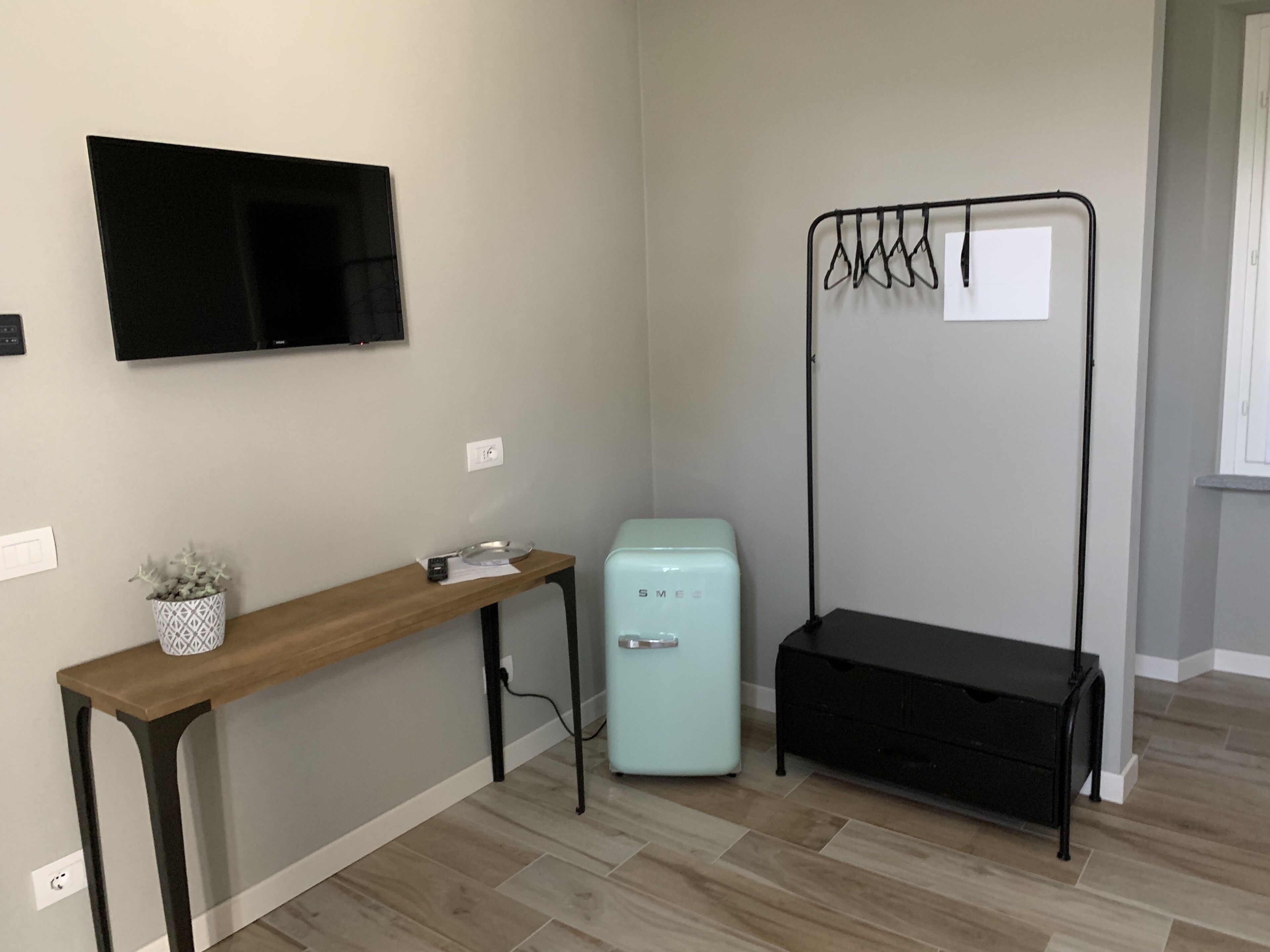 Une chambre avec un bureau en bois, un petit réfrigérateur, un téléviseur fixé au mur et un banc noir muni de crochets.