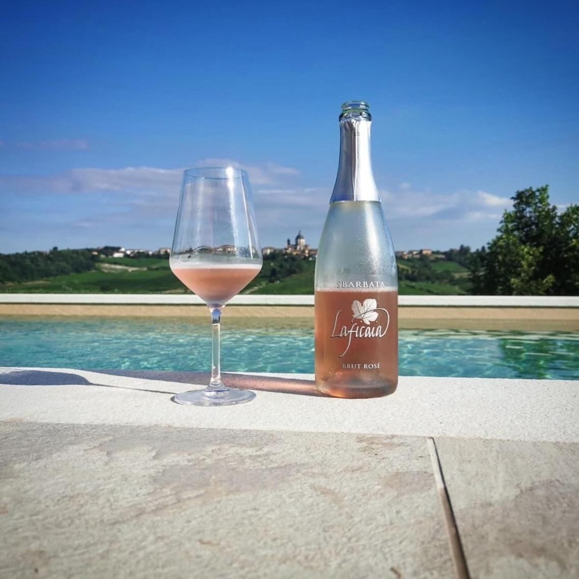 Una botella de vino Laffica y una copa sobre una mesa junto a la piscina, con vista a la piscina y al paisaje.