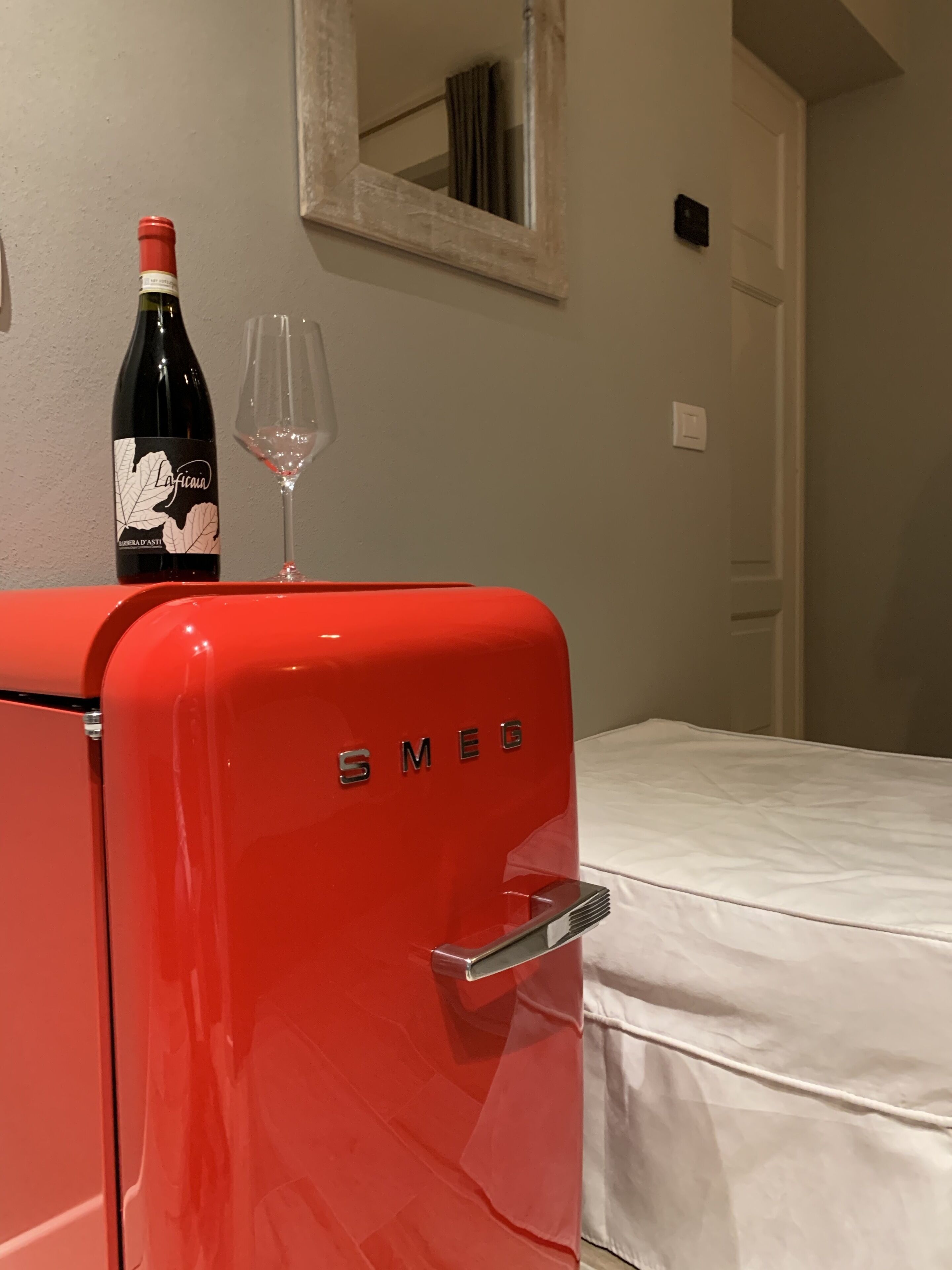 Un refrigerador vintage rojo con el nombre de la marca 'SMEG' en la puerta, una botella de vino y una copa de vino encima.
