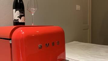 Un refrigerador vintage rojo con el nombre de la marca 'SMEG' en la puerta, una botella de vino y una copa de vino encima.