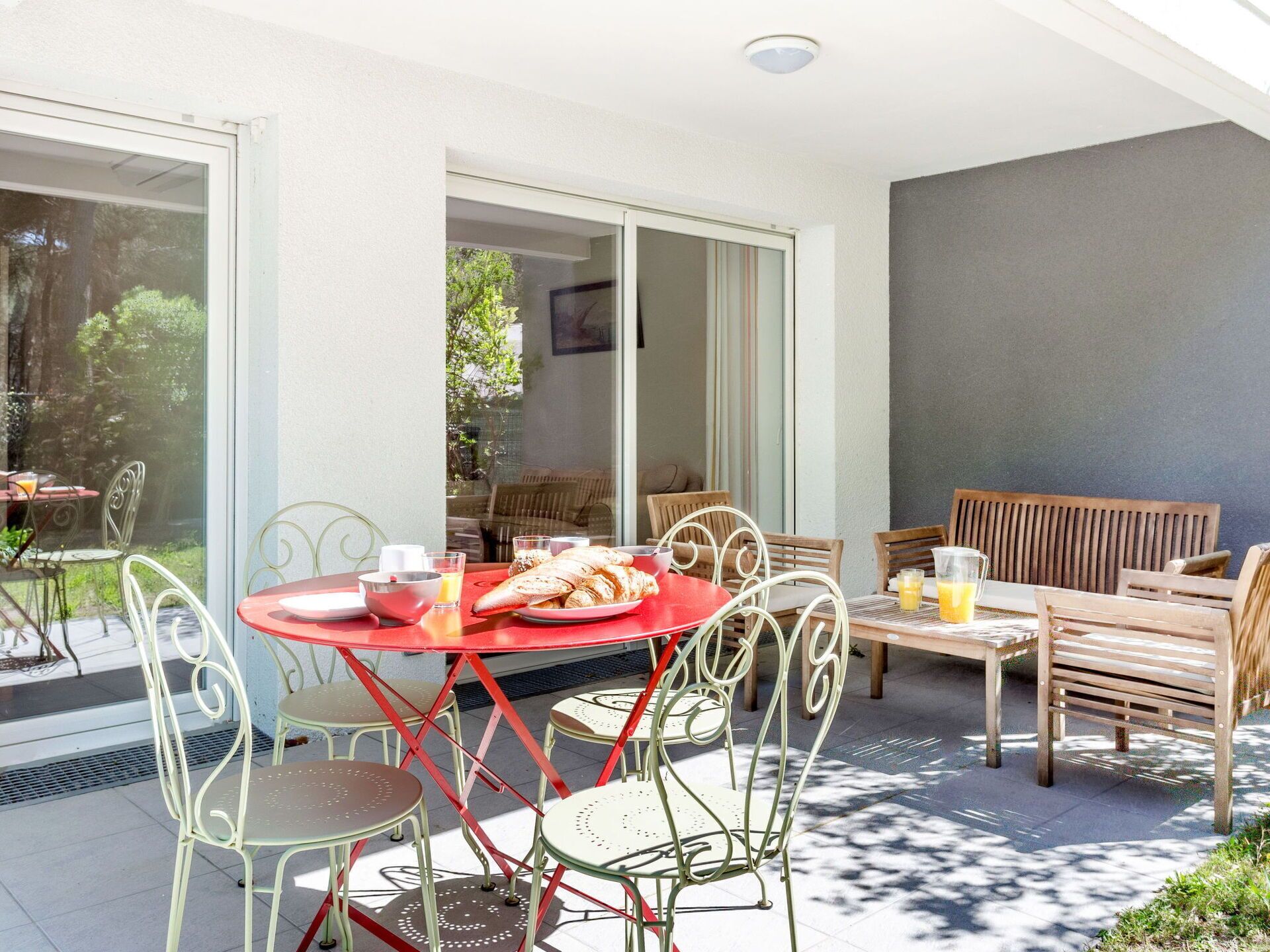 An outdoor patio with a table set for breakfast, surrounded by metal chairs and a wooden bench.