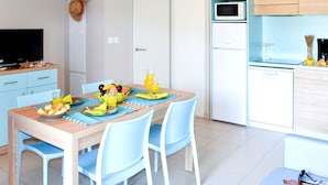 Een moderne keuken met een magnetron, oven en koelkast. Er is een eettafel met stoelen en een televisie op de achtergrond.