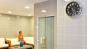 Een moderne badkamer met een douchecabine van glas, een klok aan de muur en een zithoek met een bankje en kussens.