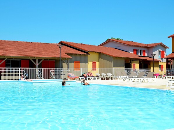 A swimming pool with lounge chairs and a building with red roofs and balconies.