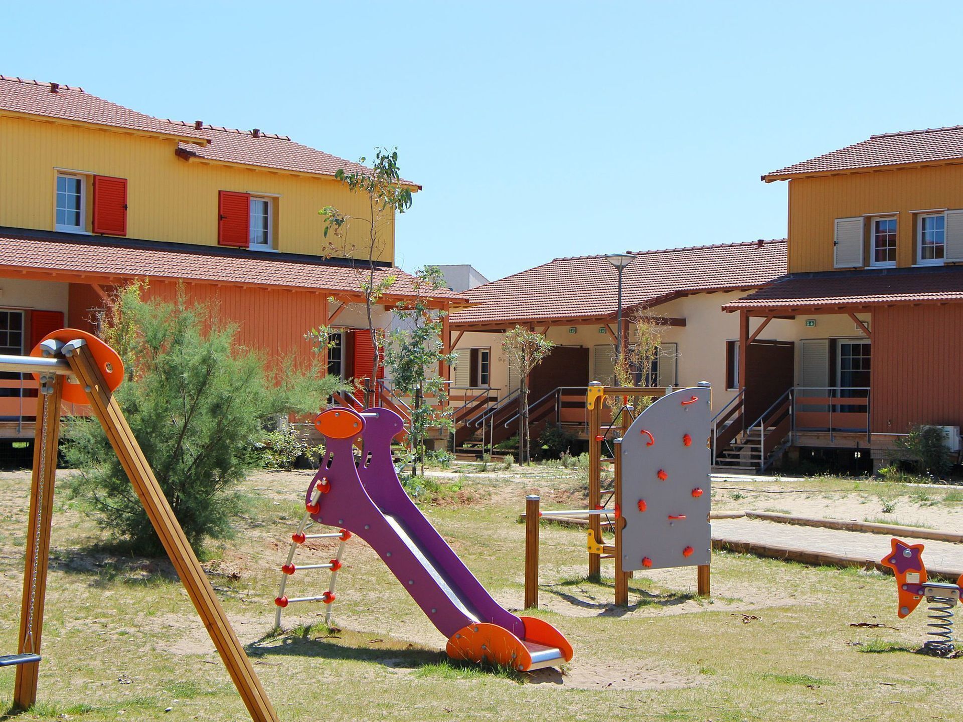 Un parc infantil amb tobogan i elements per a escalar, envoltat d'edificis amb teulades vermelles.