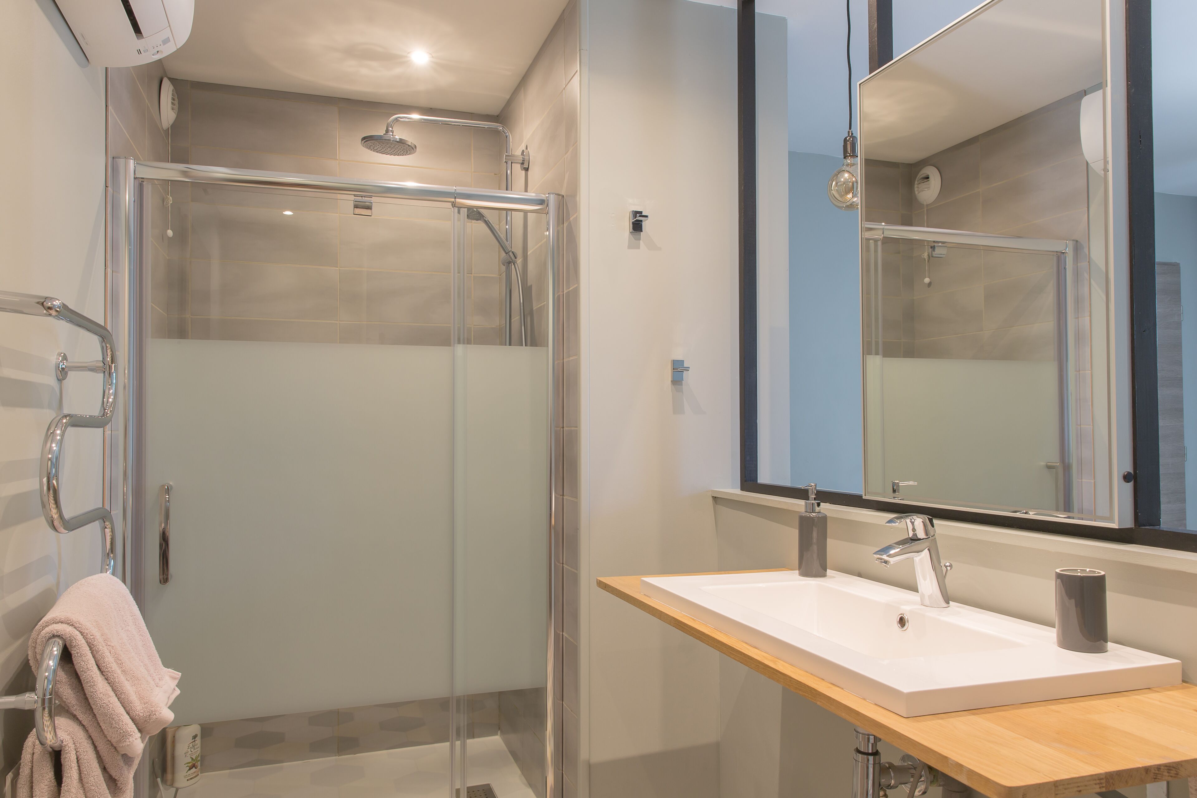 A modern bathroom with a glass-enclosed shower, a wooden vanity with a white sink, and a large mirror above the sink.