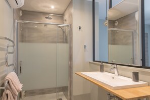 Un bagno moderno con doccia vetrata, mobile lavabo in legno e un ampio specchio sopra il lavello.