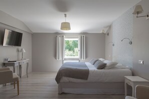 Una camera da letto con un letto, una scrivania, una sedia, una TV e una finestra con tende.