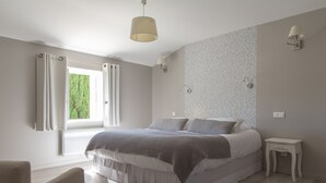 A bedroom with a large bed, a bedside table, a window with curtains, and a wall with a patterned wallpaper. - Le Mas des Alexandrins (Uzès)