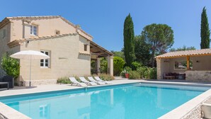 A swimming pool with lounge chairs, a pergola, and a stone building with a tiled roof. - Le Mas des Alexandrins (Uzès)