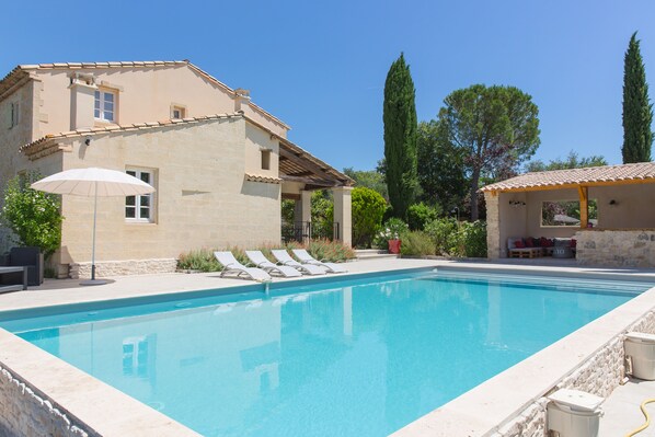 Una piscina con lettini, una pergola e un edificio in pietra con tetto in tegole.