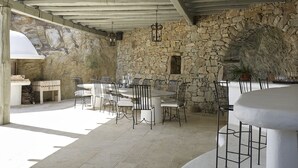 An outdoor dining area with stone walls, a stone fireplace, and a covered ceiling. - Villa Carina by Paradise Estate Mykonos : Prime Location & Endless Sea Views (Platis Gialos, Mykonos)
