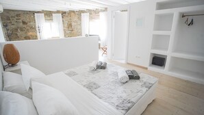 A bedroom with a large bed, a stone wall, and a wooden floor. - Villa Carina by Paradise Estate Mykonos : Prime Location & Endless Sea Views (Platis Gialos, Mykonos)