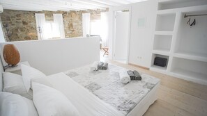 A bedroom with a large bed, a stone wall, and a wooden floor. - Villa Carina by Paradise Estate Mykonos : Prime Location & Endless Sea Views (Platis Gialos, Mykonos)