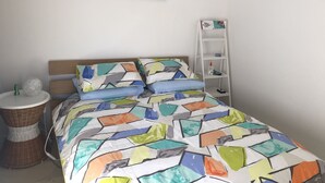 A bedroom with a bed, a wall-mounted shelf, and a wicker side table. - One of best locations at Coast. Surrounded by nature and the sound of surf. (Adelaide)