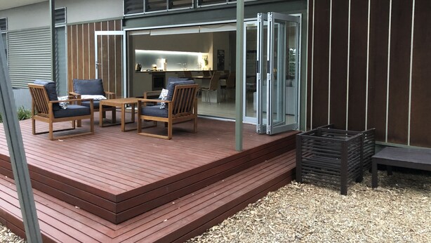 A modern outdoor patio with wooden furniture and a glass door leading to an interior space. - One of best locations at Coast. Surrounded by nature and the sound of surf. (Adelaide)
