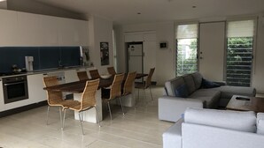 A modern kitchen with a dining area, a grey sofa, and a large window. - One of best locations at Coast. Surrounded by nature and the sound of surf. (Adelaide)