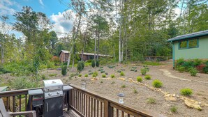 A deck with a barbecue grill, a wooden bench, and a view of a landscaped garden with trees and a small building. - Blue Ridge Retreat w/ Deck: Hike, Sip & Explore! (Asheville)