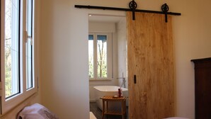 Ein Schlafzimmer mit einem Bett, einer Holztür, einem Fenster und Blick auf ein Badezimmer.