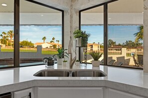 A kitchen with a large window, a stainless steel sink, and potted plants. - FIVE STAR RESORT VIBE on GOLF COURSE w/POOL & SPA (Lake Havasu)