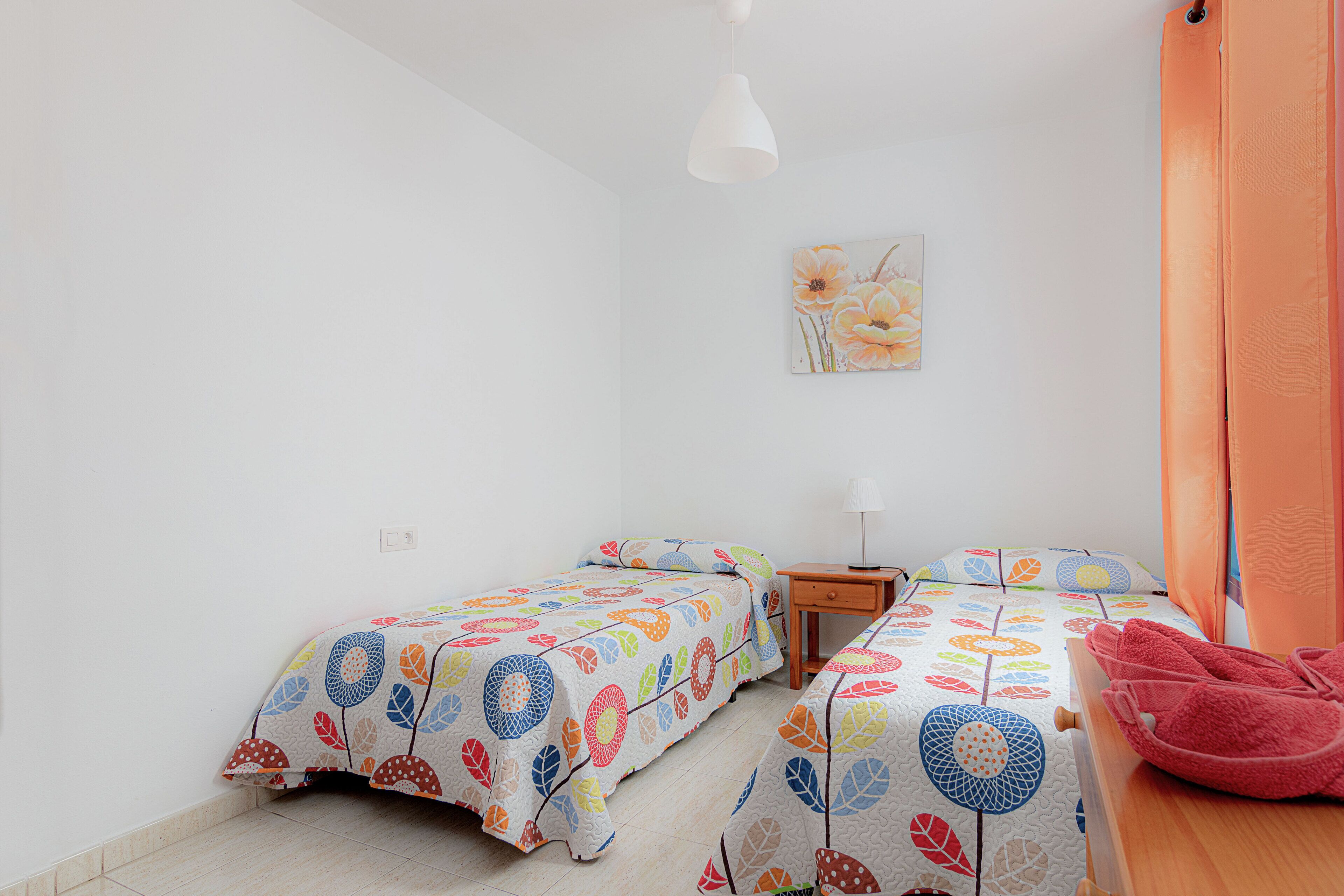 Une chambre avec deux lits, une table de chevet, une lampe et un tableau au mur.