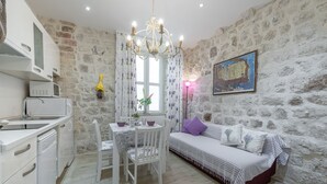 Une pièce avec un mur en pierre, un lit avec une literie à rayures, une table à manger avec des chaises, un lustre et un coin cuisine avec des appareils électroménagers blancs.