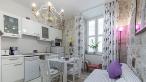 Une cuisine compacte avec des meubles blancs, une table à manger avec des chaises, un lit avec une literie à rayures et un lustre.