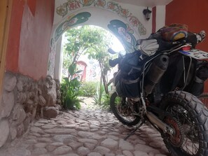 Ein Motorrad steht auf einem schmalen Steinweg mit einem Zierbogen und einer roten Mauer.