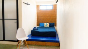 Una habitación pequeña y acogedora con cama, una silla blanca y un ventanal.