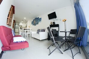 Un salon moderne avec un canapé rouge, des fauteuils noirs, un divan blanc et un coin repas comprenant une table et des chaises.