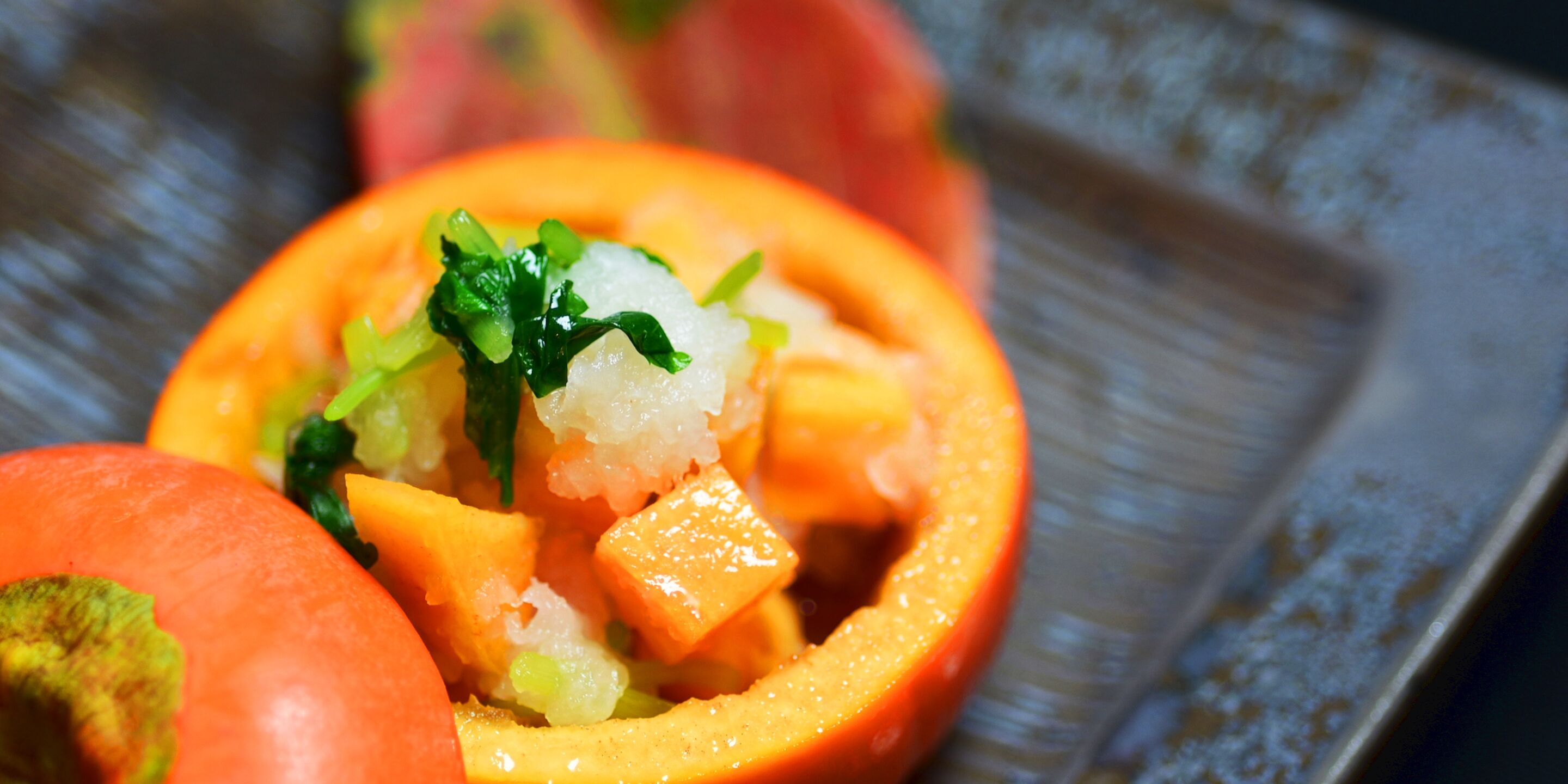 A close-up of a dish with a vibrant orange vegetable, possibly a bell pepper, filled with diced ingredients and garnished with green herbs.