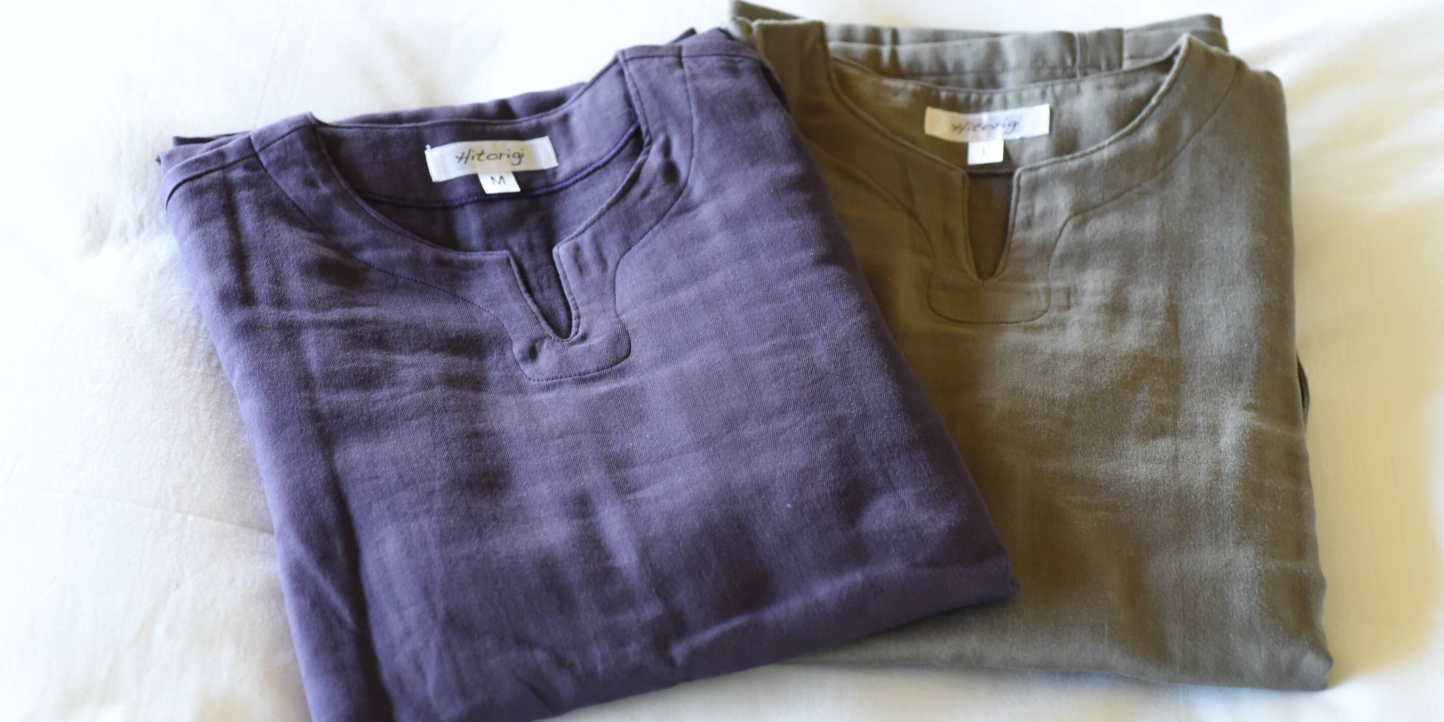 Two folded shirts on a bed.