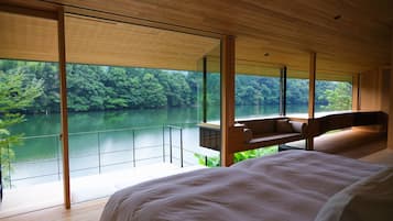 A bedroom with a large bed, a wooden bench, and a view of a lake surrounded by trees.
