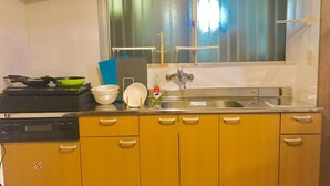 A compact kitchen with a stove, sink, and yellow cabinets. - Local Tenjin House (Fukuoka)