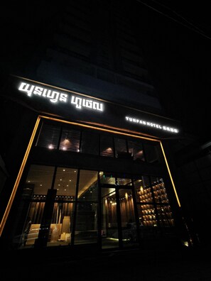 Een hotelentree met verlichte borden en grote ramen.