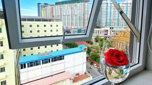 A view from a window with a glass table holding a wine glass and a red rose, overlooking a cityscape with buildings and a clear sky. - Yunfan Hotel (Phnom Penh)