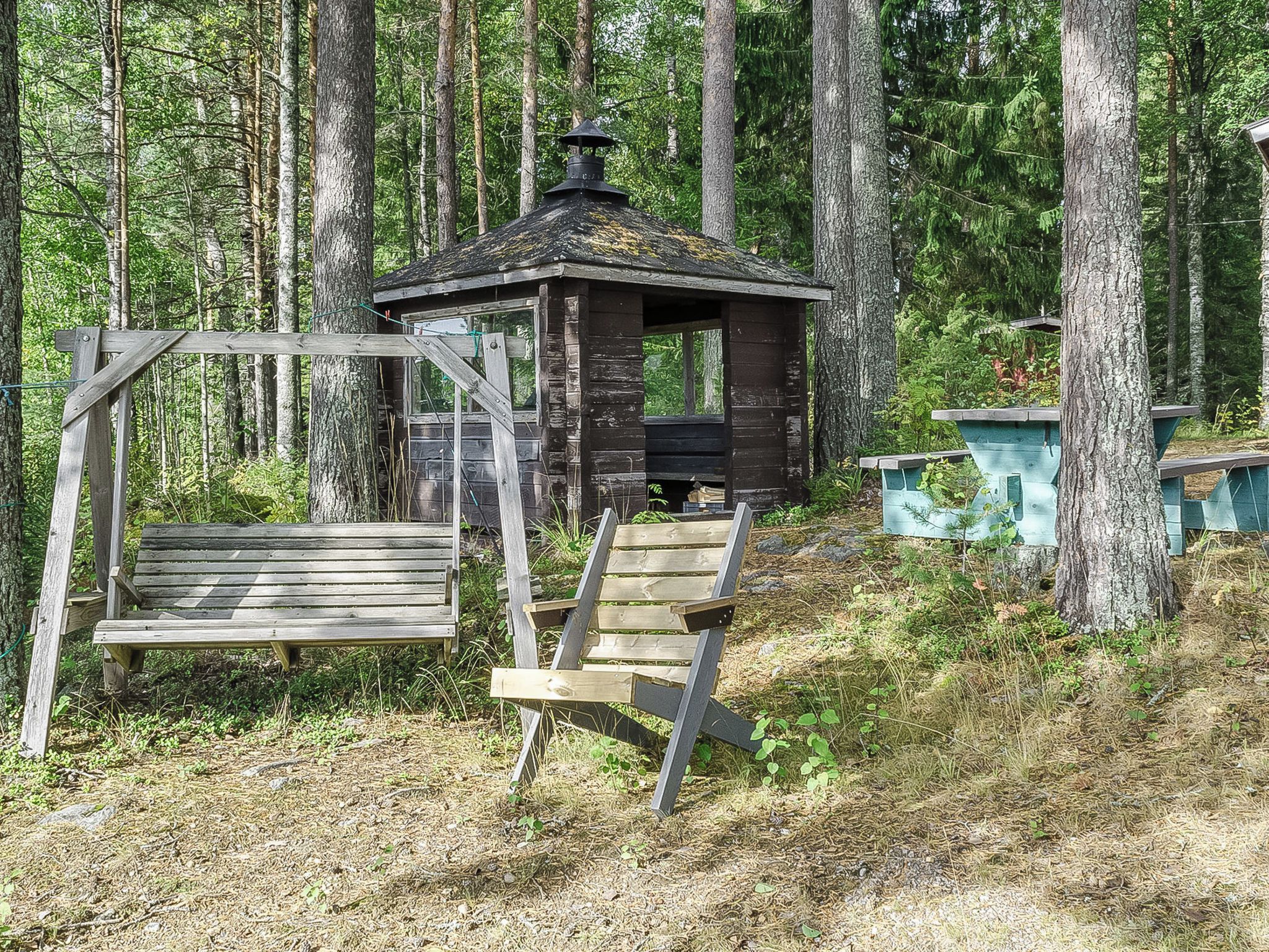A rustic wooden cabin with a chimney, surrounded by a forest. There is a wooden bench and a set of stairs leading to the cabin.