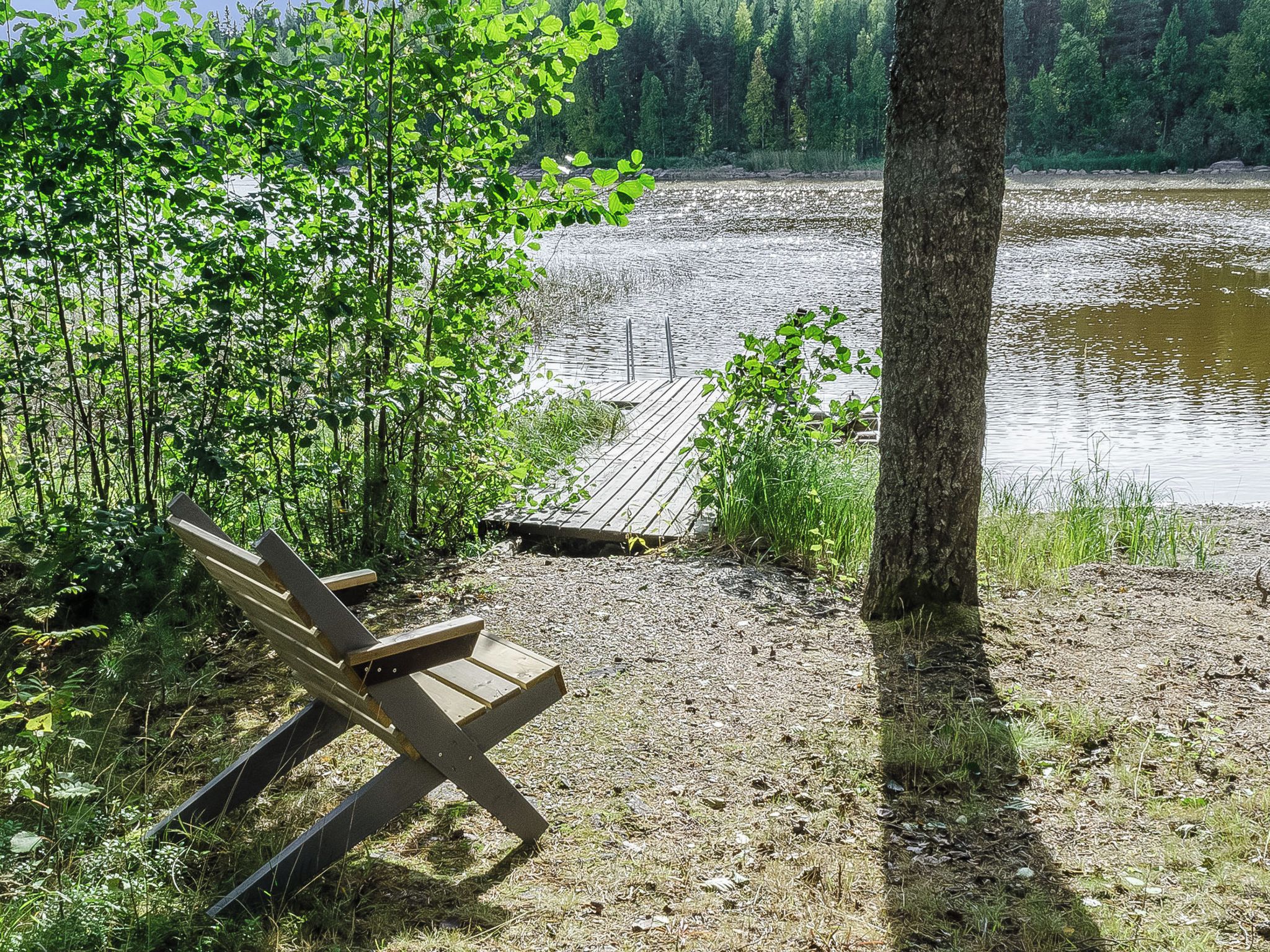 A wooden bench near a dock extending into a lake surrounded by trees.