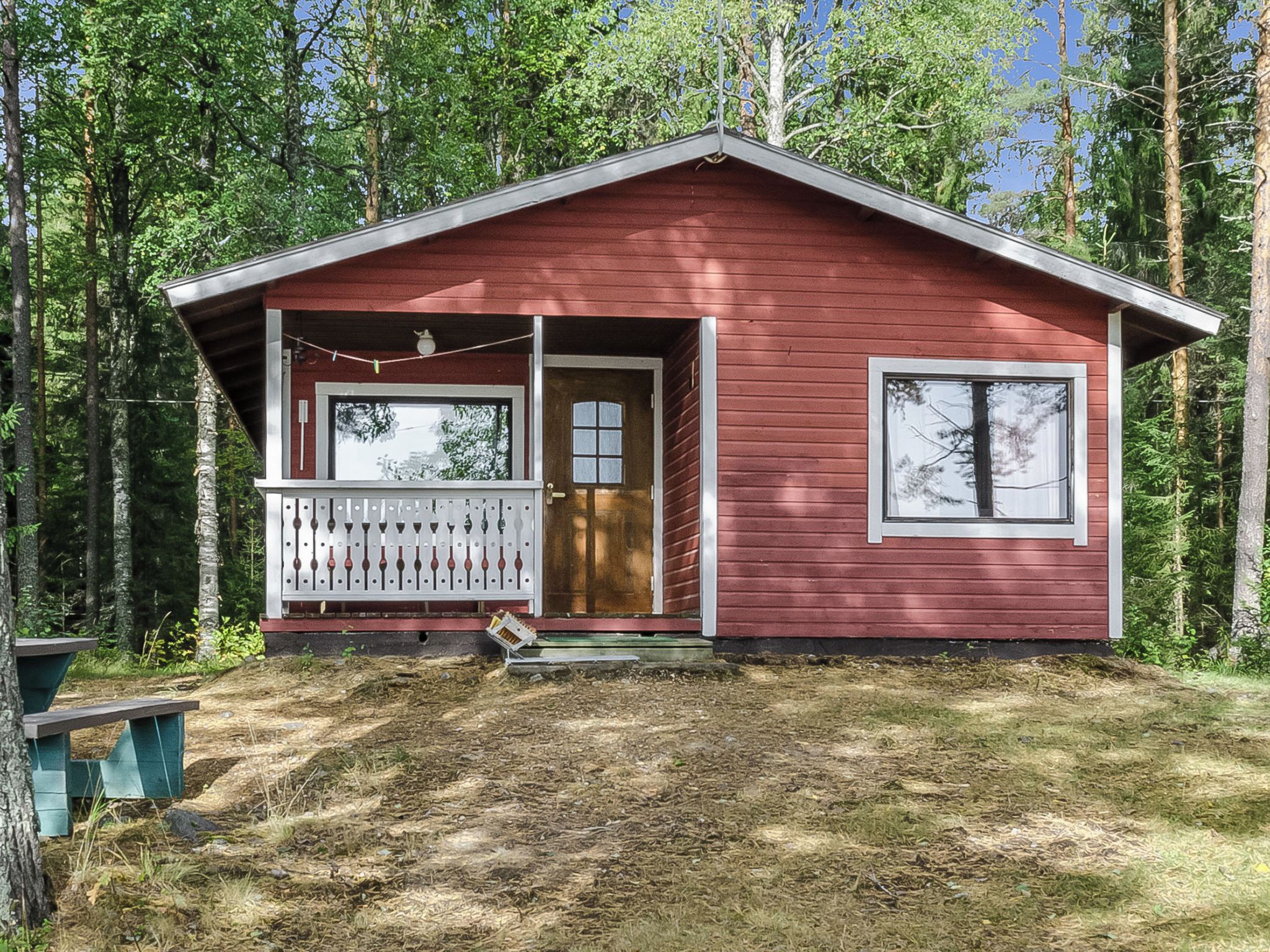 Une cabane rouge avec une véranda, une porte et une fenêtre.