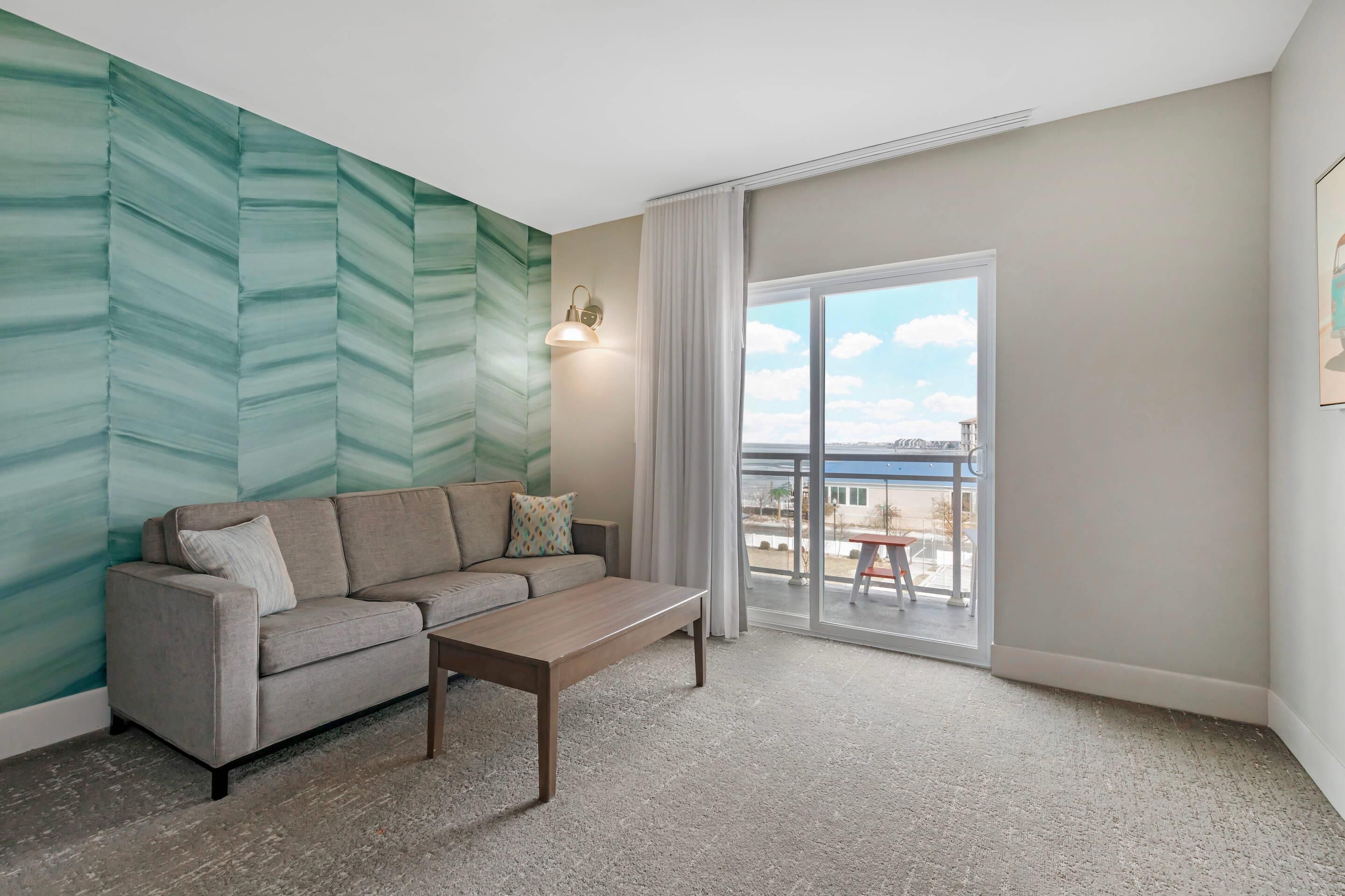 Una sala de estar moderna con un sofá, una mesa de centro, una pared con un diseño geométrico, una puerta corredera de vidrio y vistas al exterior.