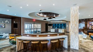 A modern bar area with a circular counter, bar stools, and a seating area with a view of bicycles outside. - Cambria Hotel Ocean City - Bayfront (Ocean City)