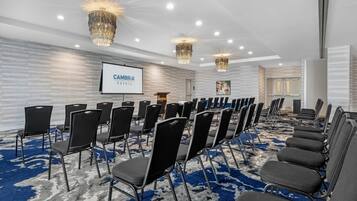 Un salón de conferencias con filas de sillas negras, una pantalla de proyector y candelabros.