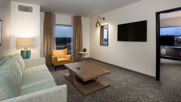 A hotel room with a sofa, armchair, coffee table, and a large window with curtains.