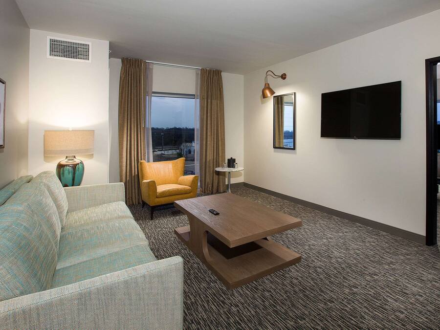 A hotel room with a sofa, armchair, coffee table, and a large window with curtains.